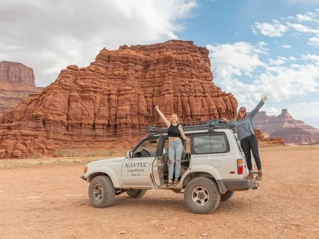 Zwei Frauen posieren begeistert neben einem 4x4-Fahrzeug in einer Wüstenlandschaft