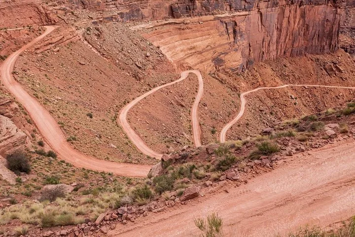 Una strada sterrata ripida e tortuosa scende lungo la parete di un canyon di roccia rossa