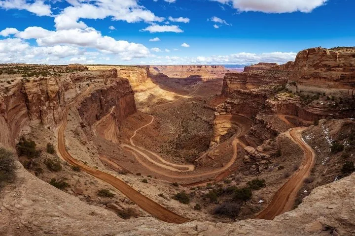 Una strada sterrata tortuosa scende in profondità in un vasto canyon desertico