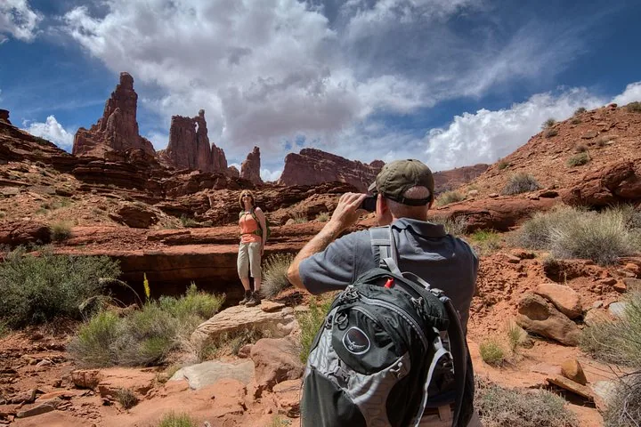 A man takes a photo of a woman standing near towering rock formations