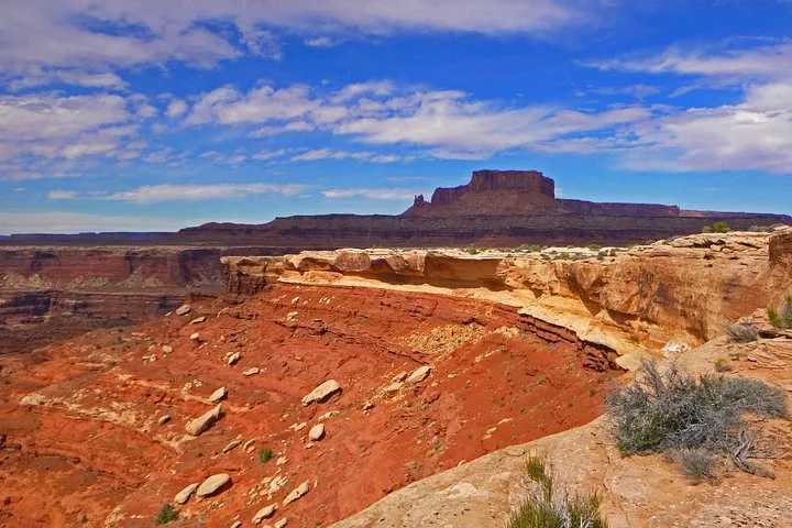 A red rock canyon wall drops down to a valley with a mesa behind