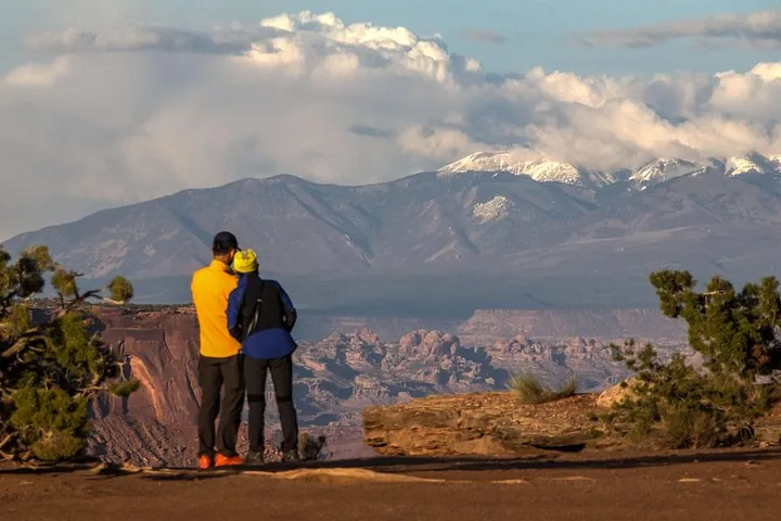 Two people look out over a canyon landscape towards snow-capped mountains